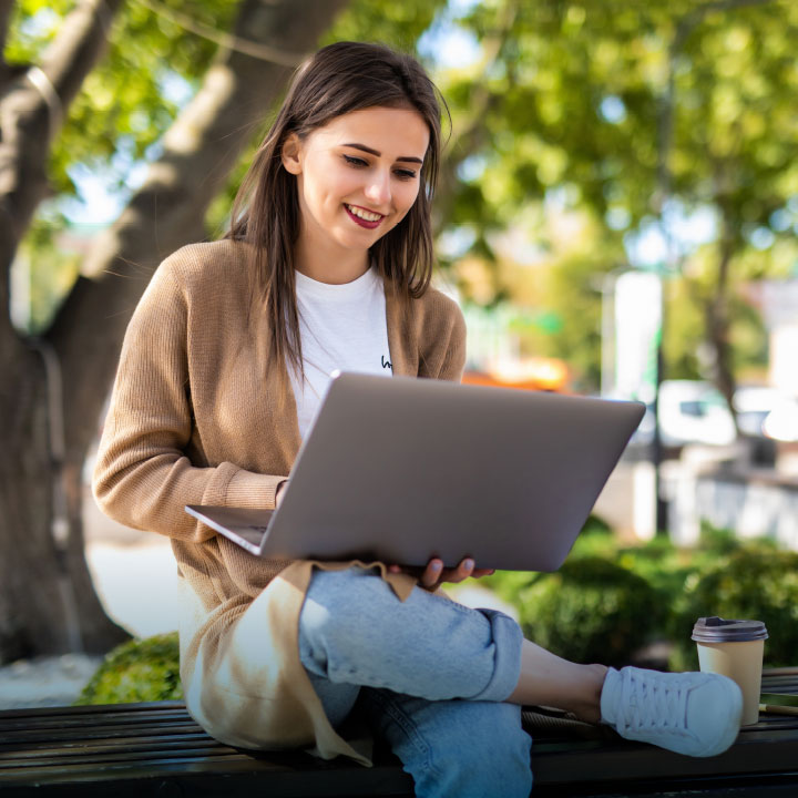 Eine Frau sitzt im Freien am Laptop und arbeitet mit Hilfe einer Cloud